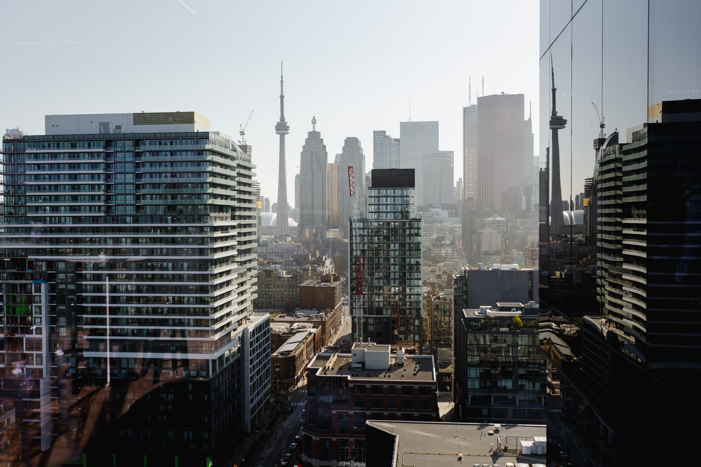 Aerial view of a cityscape featuring high-rise buildings, the CN Tower, and glass reflections on the right side, with a clear sky in the background. This stunning scene captures the essence of corporate photography at its finest.