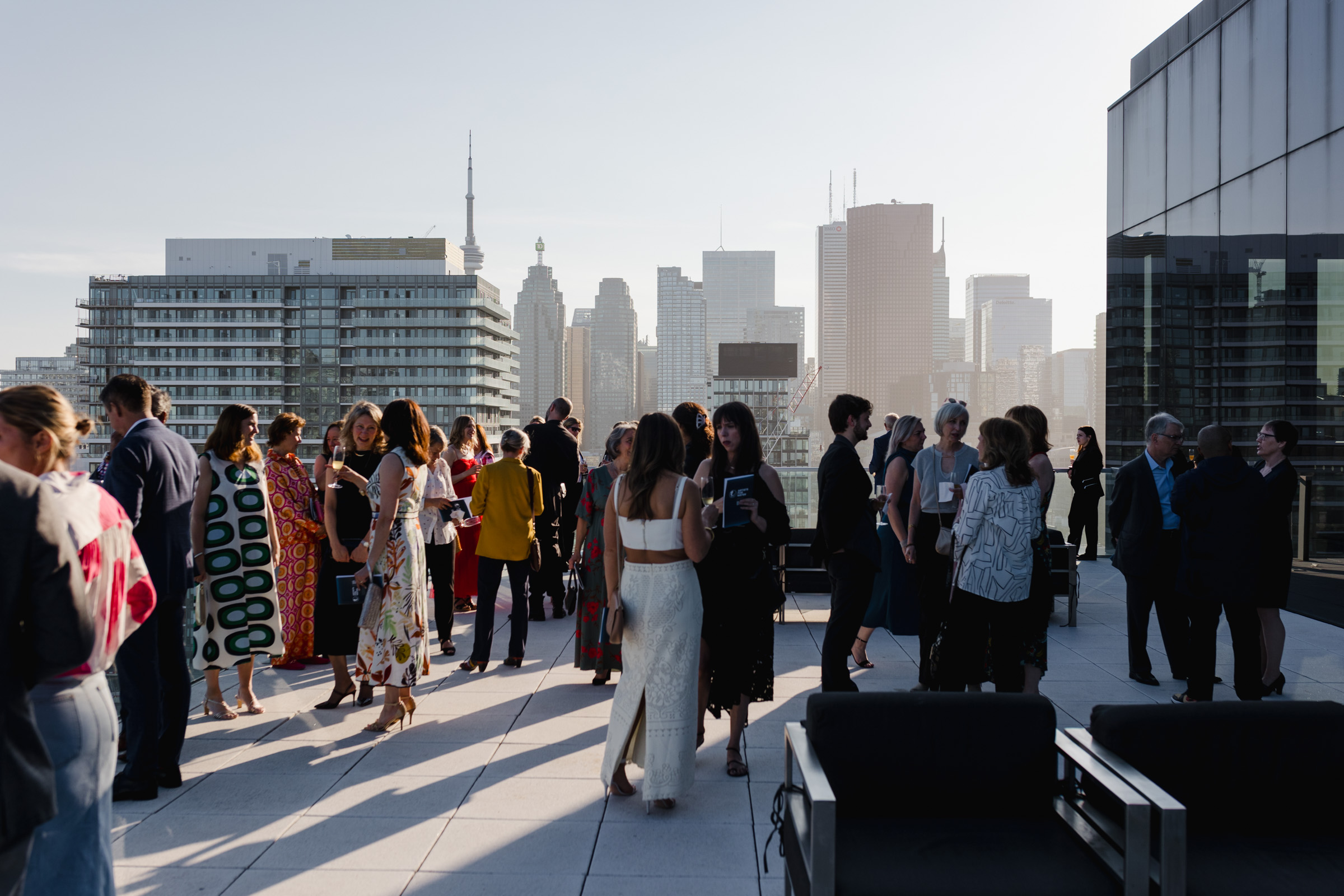 A group of people socializing on a rooftop terrace with a city skyline in the background, under clear skies during daylight, makes for perfect event photography.