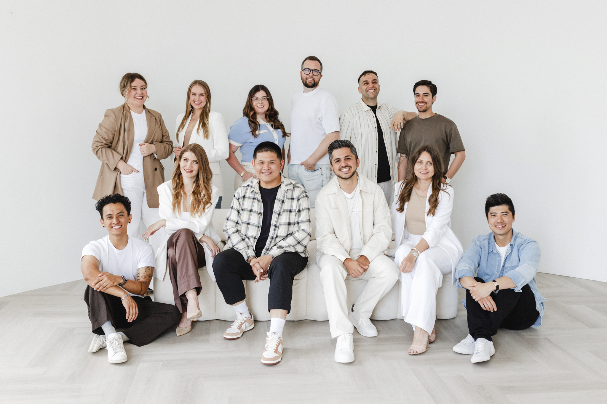 A creative team of thirteen people, casually dressed, poses together in a brightly lit room with a white background.