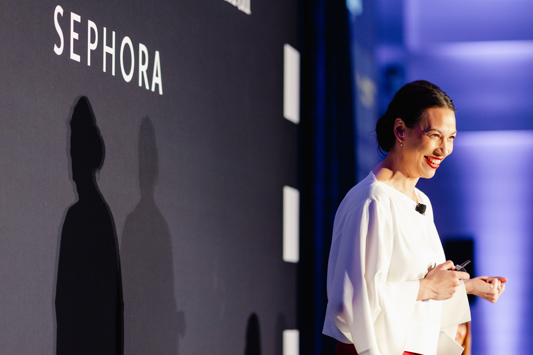 A person stands on stage in front of a Sephora-branded backdrop, smiling and holding a clicker, exemplifying the essence of corporate photography.