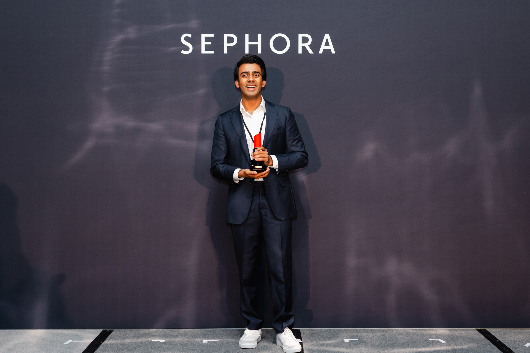 A man in a dark suit holding an award stands in front of a Sephora backdrop, exemplifying top-notch corporate photography.