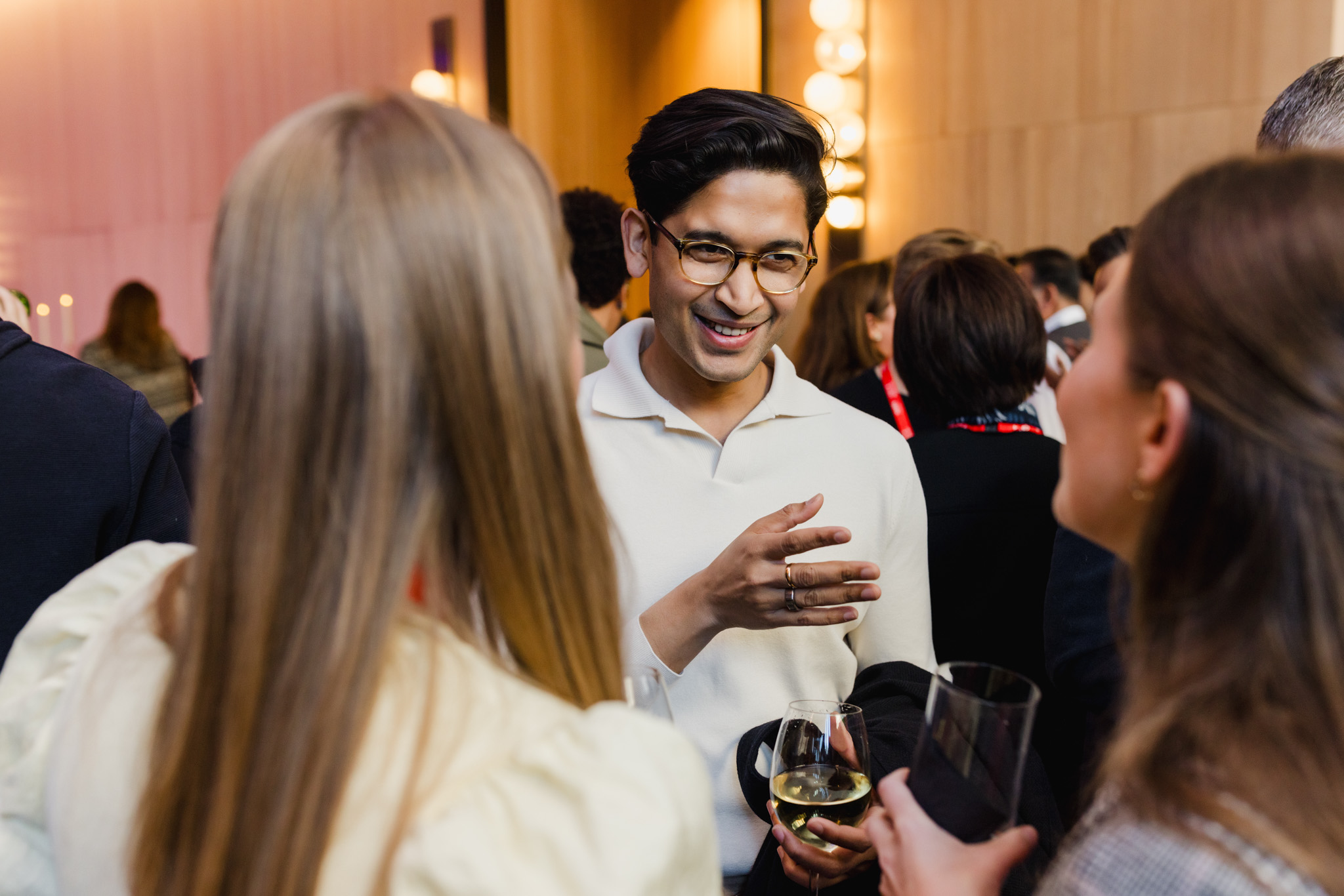 A person is smiling and conversing with two others at a social event. They are holding drinks and appear to be enjoying the conversation in a warmly lit room, perfectly captured through corporate photography.